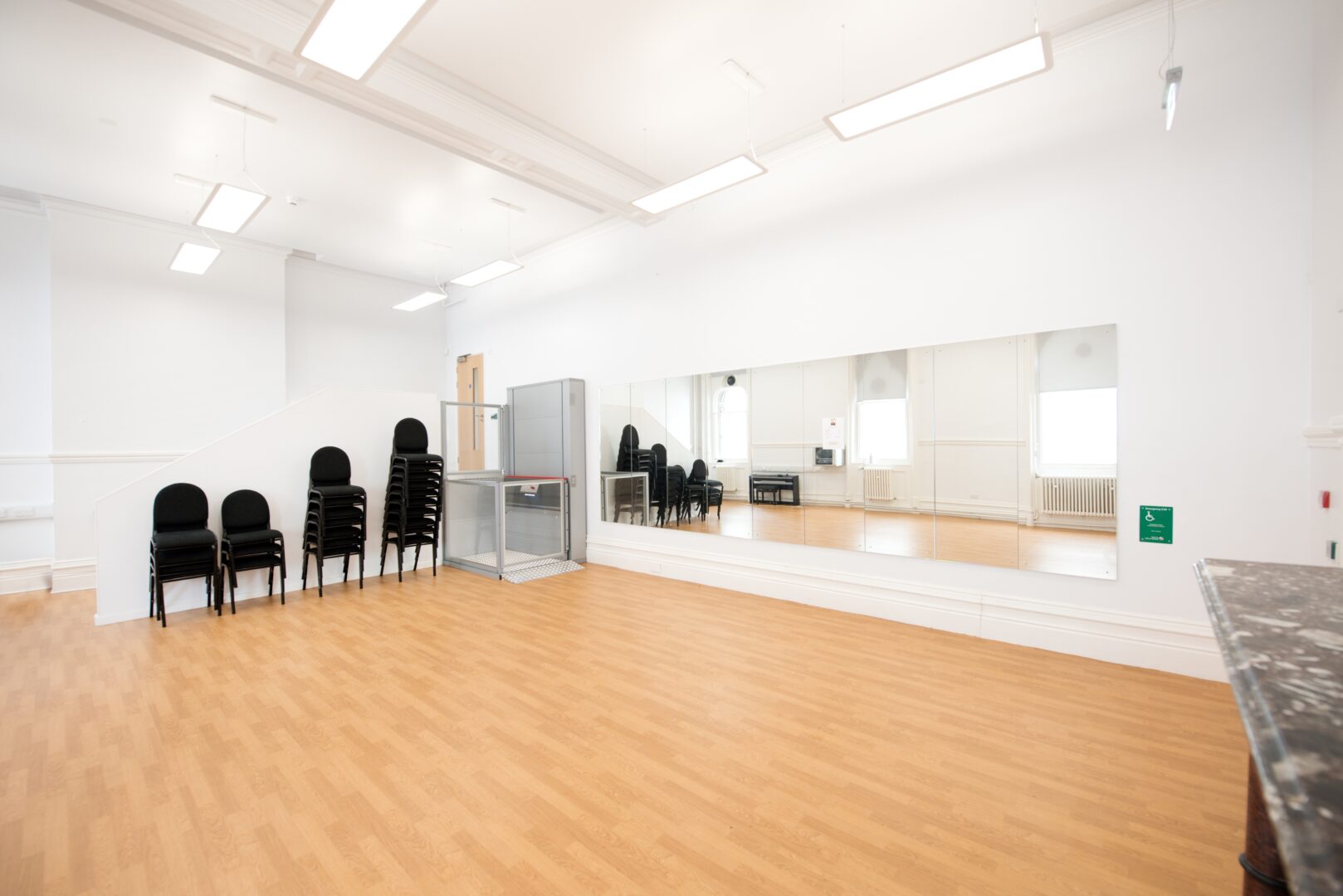 large bright room with mirrors on the wall and chairs stacked up against the wall